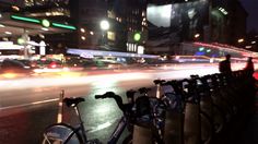 there are many bikes parked on the side of the street at night time, with blurry lights in the background