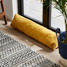 a yellow pillow sitting on top of a wooden floor next to a potted plant