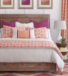 a bed with pink and orange pillows in a bedroom next to two pictures on the wall