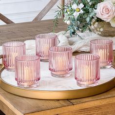 six pink glass tumblers on a tray with flowers and greenery in the background