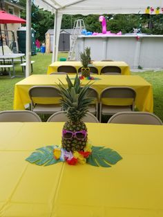 a pineapple sitting on top of a yellow table covered in flowers and sunglasses next to chairs