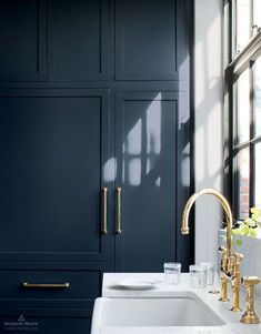 a white sink sitting under a window next to a tall cabinet with gold handles and knobs