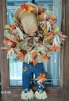 a scarecrow door hanger decorated with fall leaves and a cowboy's hat