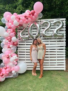 two women standing next to each other in front of a sign with balloons on it