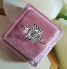 an emerald and diamond ring in a pink velvet box with white flowers on the side