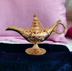 a golden teapot sitting on top of a blue velvet covered bed next to a pink pillow