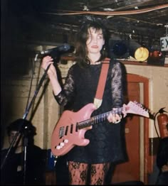 a woman standing in front of a microphone while holding a guitar