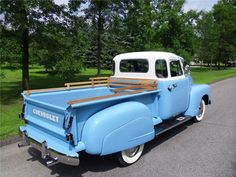 an old blue and white pick up truck parked on the side of the road with trees in the background