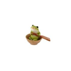 a frog sitting on top of a wooden bowl with chopsticks in its mouth