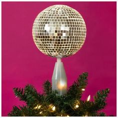 a disco ball on top of a christmas tree in front of a pink background with lights