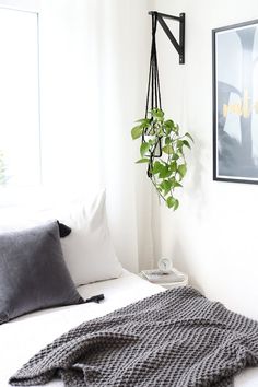 a bed with white sheets and pillows in a room next to a plant on the wall