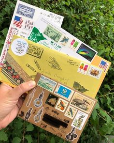 a person holding an envelope full of stamps and stickers in front of some bushes