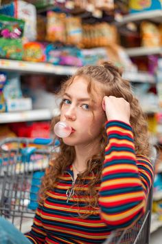 a woman sitting in a shopping cart blowing bubbles into her nose while looking at the camera