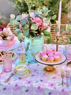 a table topped with lots of cupcakes and pink flowers next to a blue jar