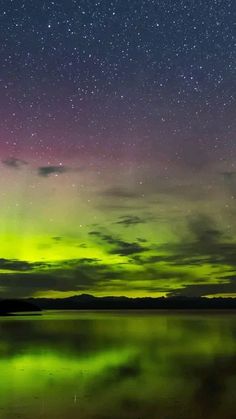 the sky is lit up with green and purple lights as it reflects in the water