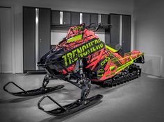 a red and black snowmobile with neon green lettering on the front parked in a garage