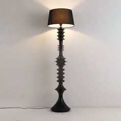 a black lamp with a brown shade on it and a white wall in the background