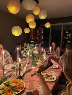 a group of people sitting around a table with plates of food and candles in front of them