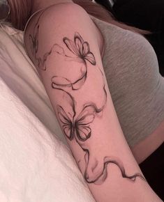 a woman laying in bed with a tattoo on her arm that has flowers and butterflies all over it