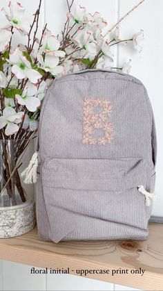 a gray backpack sitting on top of a wooden shelf next to a vase with flowers