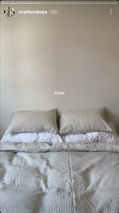 a bed with two pillows on top of it and a white wall in the background