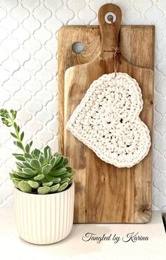 a wooden cutting board with a crocheted heart hanging on it next to a succulent plant