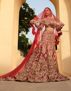 a woman in a red and gold bridal gown standing under an archway with her hands on her hips