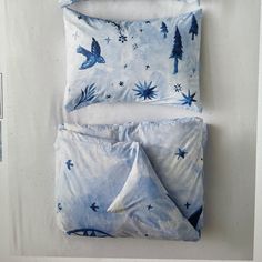 two pillows with blue and white designs on them, one is folded up to the side