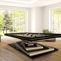 a pool table in the middle of a room with large windows and wood flooring