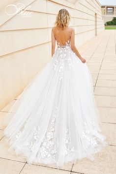 a woman in a white wedding dress standing on the side of a building with her back to the camera