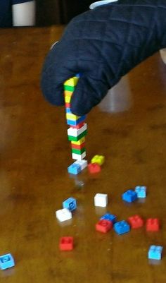 a person is playing with legos on the wooden table and reaching for them to grab one