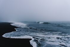 the ocean waves are coming in to shore on a foggy, overcast day