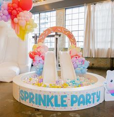 an inflatable water slide with balloons and streamers on the top for a birthday party