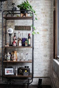 a shelf filled with bottles and glasses next to a window in a brick walled room