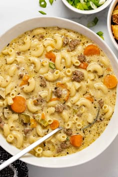 a white bowl filled with pasta and meat soup next to bowls of bread on the side