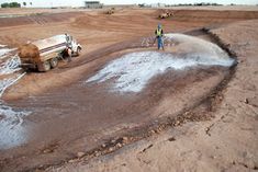 two men standing next to a truck on top of a dirt covered field with water coming out of it