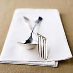 a fork and knife on top of a white napkin next to an empty plate with two forks sticking out of it