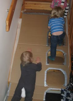 two children playing on cardboard stairs in the house with their hands up and feet down