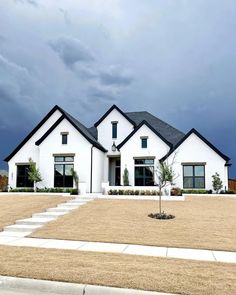 a white house with black roof and windows on a cloudy day in front of a blue sky