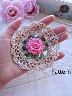 a hand is holding a crocheted doily with a pink rose on it