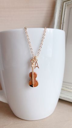 a white cup with a gold necklace and a violin charm hanging from it's side