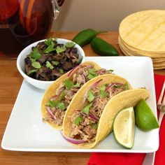 three tacos with meat, onions and cilantro on a white plate next to a lime