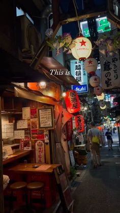 people walking down an alley way at night with signs hanging from the ceiling and lights above them