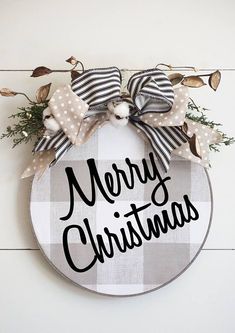 a merry christmas sign hanging on the side of a wooden wall with bows and greenery