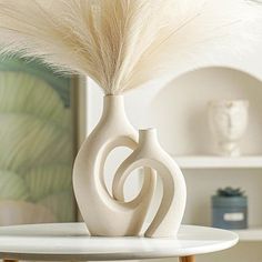 a white vase sitting on top of a table next to a feather in it's mouth