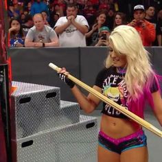 a woman holding a baseball bat on top of a wrestling ring in front of a crowd