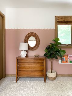 a living room with pink walls and a wooden dresser next to a mirror on the wall