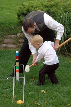 a man playing with a child in the grass while holding a baseball bat and hitting a ball