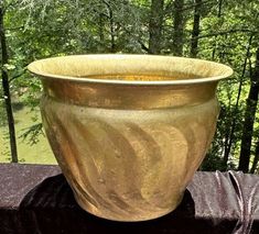 a large gold vase sitting on top of a wooden table next to a forest filled with trees