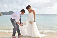 a man and woman standing on top of a beach next to the ocean holding hands